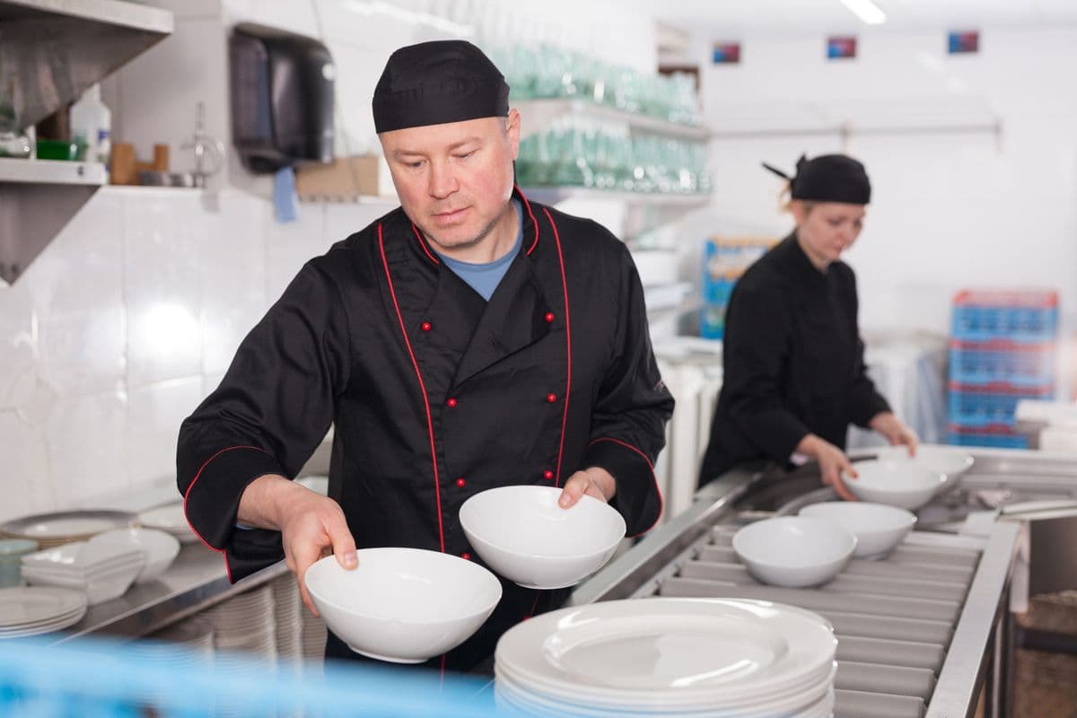 Kitchen worker arranging cleaned dishes, preparing for serving