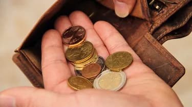 A hand holding several euro coins with an open brown leather wallet in the background.